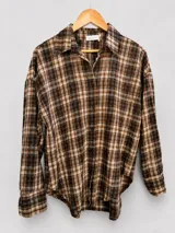 Camisa de manga larga con estampado a cuadros en tonos marrones, beige y negro. Presenta cuello clásico, cierre frontal con botones y corte holgado.