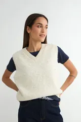Chaleco de punto color crema con escote en V, sin mangas y diseño decorado con pequeñas perlas aplicadas en toda la superficie.