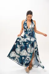Vestido largo con escote halter profundo y diseño sin mangas. Presenta un estampado difuminado en tonos azules, celestes, blancos y grises, con corte ajustado en el torso y una falda larga con vuelo.
