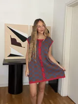 Vestido corto tejido en jacquard de algodón, con diseño a cuadros en tonos azul y marrón, cuello redondo con ribete rojo y cierre frontal con botones.