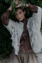 Saco de punto color crudo con diseño de flecos en el frente y mangas, cierre frontal con botones y cuello redondo.