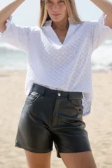 Short de cuero negro, estilo jean, con tiro alto y cierre frontal con botón plateado.