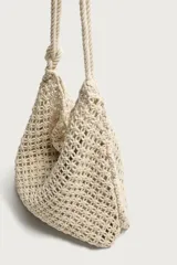 Bolso de hombro confeccionado en tejido trenzado de algodón con diseño de macramé, asa de hombro con detalle de nudo y bolsillo interior plano.