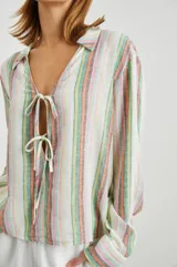 Blusa de lino a rayas verticales de color blanco, naranja, verde y marrón, con cuello camisero, mangas largas con puños y lazos ajustables en el escote.