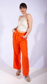 Top corto de satén color beige con escote cuadrado y breteles formados por cadenas metálicas doradas que se extienden hacia la espalda.