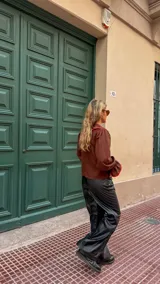 Camisa de color marrón chocolate con cuello Peter Pan y puños con volados, ambos detalles resaltados con un ribete en color rojo. Presenta cierre frontal con botones rojos.