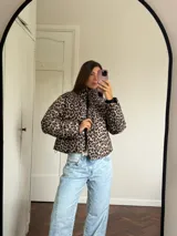 Campera puffer con estampado de leopardo en tonos blanco y negro, cuello alto, cierre frontal y bolsillos laterales.
