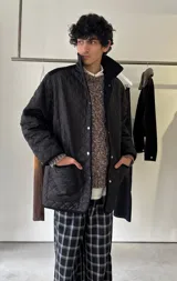 Campera capitoneada de color negro con diseño acolchado en forma de rombos, cierre frontal con botones a presión y bolsillos frontales amplios. Presenta un corte holgado y detalles de terminación en contraste.
