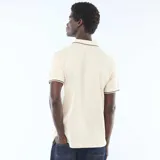 Remera polo de piqué de algodón color beige claro, de manga corta, con cuello y bordes de mangas en ribete negro y blanco.