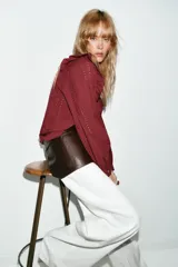 Blusa de manga larga con cuello redondo, volantes en los hombros y detalle de jaretas frontales. Presenta bordados perforados en toda la prenda y cierre posterior con botones ocultos.