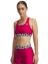 Top deportivo Under Armour de soporte medio, color fucsia con banda elástica inferior negra con el logo de la marca en blanco. Presenta diseño de espalda cruzada y tejido técnico de secado rápido.