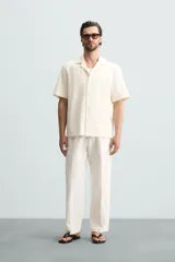 Camisa de corte regular fit confeccionada en tejido con estructura de color negro. Cuenta con cuello bowling, manga corta, aberturas laterales en el bajo y cierre frontal de botones.