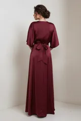 Vestido largo tipo kimono confeccionado en satén color bordó, con escote en V cruzado, mangas amplias y lazo ajustable en la cintura. Presenta una falda fluida con abertura lateral.