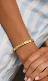 Brazalete rígido de acero dorado con textura martillada y diseño de eslabones circulares unidos.