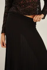Falda larga de punto en color negro, con diseño plisado y acabado con sutil brillo metalizado. Presenta un corte acampanado con caída fluida.