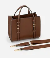 Cartera satchel mediana de color marrón, confeccionada en poliuretano con diseño estructurado, costuras en contraste y herrajes metálicos dorados. Cuenta con doble asa de mano, correas decorativas verticales con hebillas en la parte frontal y una correa larga ajustable y desmontable para llevar al hombro o cruzada.