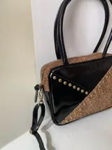 Cartera rígida negra con detalles en rojo y tachas plateadas. Tiene herrajes y cierre metálico plateado marca YKK, asa fina para llevar al hombro o en la mano y correa larga extra regulable. El interior es forrado, tiene un bolsillo con cierre enmarcado en cuero, y un segundo bolsillo plaqué.