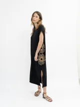 Vestido largo de color negro, con corte holgado, mangas cortas y tajo lateral. Presenta un diseño bordado de dos flores grandes en el lateral de la falda.
