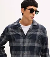 Camisa de manga larga confeccionada en franela de algodón, con cuello bowling y cierre frontal de botones. Presenta un diseño de estampado a cuadros en tonos azul marino y gris, con un corte regular.