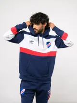 Canguro con capucha de Umbro del Club Nacional de Football, con diseño de bloques de color en azul, blanco y rojo. Presenta bolsillo frontal tipo canguro, cordones ajustables en la capucha y logos bordados del club y la marca.