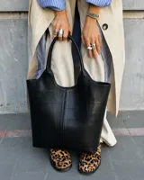Cartera tipo tote bag de eco cuero negro, con diseño de paneles pespunteados y doble asa larga para hombro.
