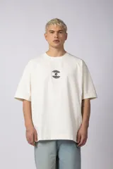 Remera de corte oversize confeccionada en algodón premium de gramaje pesado, color crudo. Presenta un bordado frontal pequeño en el centro del pecho con un diseño de dos árboles unidos por sus raíces y un parche estampado en la espalda con una silueta de mano fusionada con ramas.