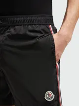 Short de baño negro con cintura elástica y cordón ajustable. Presenta una franja tricolor (rojo, blanco y azul) en los laterales y el logo de Moncler en el bajo.