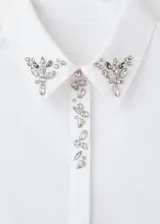 Camisa de popelín de algodón color blanco, con diseño recto, cuello camisero clásico y detalle de cristales decorativos en el cuello. Presenta cierre de botones oculto y manga larga con puños abotonados.