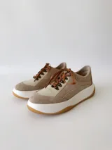 Championes de cuero color visón con cordones marrones, suela blanca y base color caramelo.