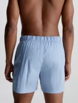 Bañador corto de largo medio Calvin Klein CK Nylon, color celeste, con cintura elástica, cordón ajustable, cinturón de cinta con hebilla y logo, bolsillos laterales y bolsillo trasero con cremallera.