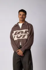 Campera tejida de punto con cierre frontal completo, cuello tipo polo y diseño con franja horizontal en contraste con estampado gráfico. Presenta puños y ruedo acanalados, con corte holgado.