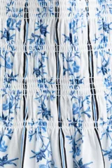 Vestido corto de algodón con sección superior fruncida y pollera con vuelo, sin mangas, con escote redondo al frente y en U en la espalda, con estampado combinado de rayas y motivos florales en tonos azules sobre fondo blanco.