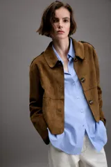 Chaqueta corta de efecto ante en color marrón, con cuello solapa, manga larga y trabillas en los hombros. Presenta cierre frontal con botones y bolsillos delanteros de doble vivo.