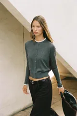 Chaqueta de punto color beige, de manga larga y corte corto, con cuello redondo y puños terminados en puntilla blanca a contraste.