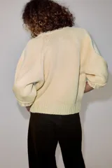Chaqueta de punto color amarillo claro, con cuello redondo, mangas abullonadas por debajo del codo y cierre frontal con botones oscuros.