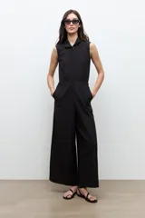 Mono largo negro sin mangas, con cuello solapa, cierre frontal con botones y detalle de vainillas en los hombros. Cuenta con cintura elástica y bolsillos laterales.