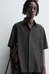 Camisa de manga corta con corte relajado, confeccionada en tejido fluido con mezcla de lyocell. Presenta cuello solapa, cierre frontal con botonadura oculta por solapa y aberturas laterales en el bajo.