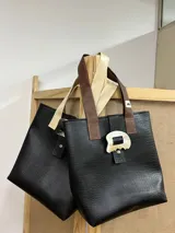 Bolso tipo tote bag negro con textura símil cuero de cocodrilo, doble asa corta color marrón y beige, y cierre con broche metálico con forma orgánica.