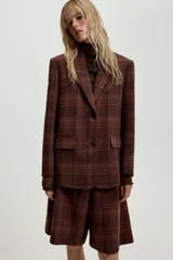 Blazer Zara de cuello solapa y manga larga, con estampado de cuadros en tonos marrones y rojizos. Presenta cierre frontal con dos botones y bolsillos delanteros con solapa.