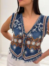 Chaleco corto en denim azul con detalle desflecado y bordado artesanal en tonos celeste y dorado. Estilo boho chic con escote en V, ideal para combinar con prendas básicas y elevar tu look.