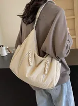 Bolso tipo hobo de tela color beige, con correa ancha ajustable, bolsillos frontales con cierre decorativo y forro interior.