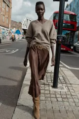 Falda midi plisada de tiro alto color marrón, con cinturón ancho de color beige y hebilla metálica cuadrada. Cierre lateral con cremallera oculta.