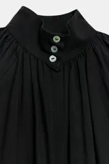 Camisa de algodón color negro, con cuello subido, manga larga terminada en puño ancho y bajo ajustable con cordones. Cuenta con cierre delantero con botones ocultos por solapa y detalles fruncidos.