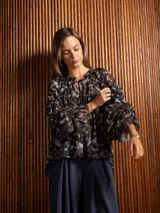 Blusa de gasa con estampado abstracto en tonos oscuros, cuello redondo con lazo ajustable, corte holgado con frunces y mangas largas abullonadas con puños elásticos.