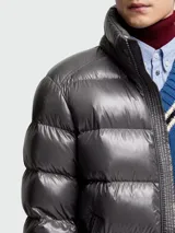 Campera corta de plumas Moncler modelo Maya, con acabado brillante, diseño acolchado horizontal, capucha integrada y cierre frontal con cremallera.
