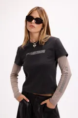 Remera de diseño superpuesto que combina una remera de manga corta en color negro con estampa frontal y mangas largas en color gris topo. Presenta un estilo urbano y moderno con corte holgado.