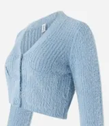 Cardigan cropped de punto color rosa claro, con textura de pelito, cuello en V, mangas largas, cierre frontal con botones y bolsillos delanteros.