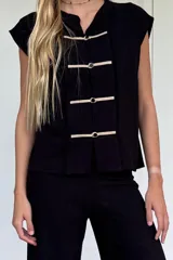 Blusa sin mangas color beige claro, confeccionada en lino tusor. Presenta cuello mao y cierre frontal con tres nudos chinos blancos. Los bordes de la abertura frontal tienen un acabado deshilachado.