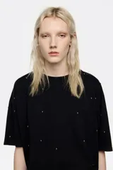 Remera de corte boxy en color negro, con escote redondo y manga corta recta. Presenta detalles de remaches metálicos distribuidos por toda la prenda.