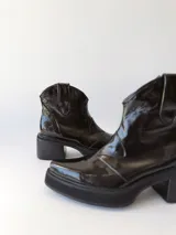 Botas texanas negras de cuero charol con caña baja, punta fina y tacón cuadrado.